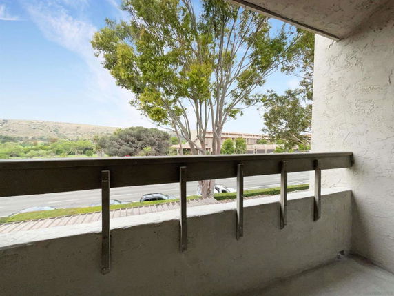 View from a balcony overlooking a street with trees and distant hills.