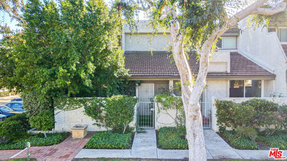 Front view of a two-story house with a gated entrance and surrounding greenery.