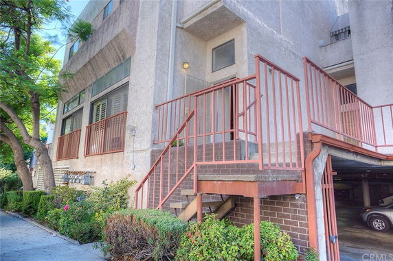 Front view of a multi-story building with an entrance staircase and parking area underneath.