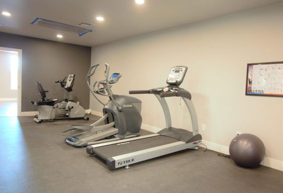 Room with exercise equipment including a treadmill, elliptical, and stationary bike.