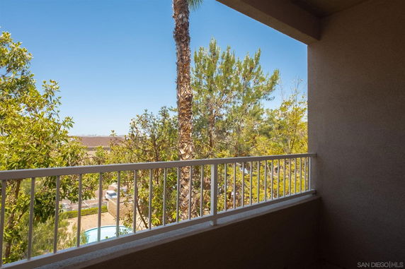 View from a balcony with trees and a clear sky visible.