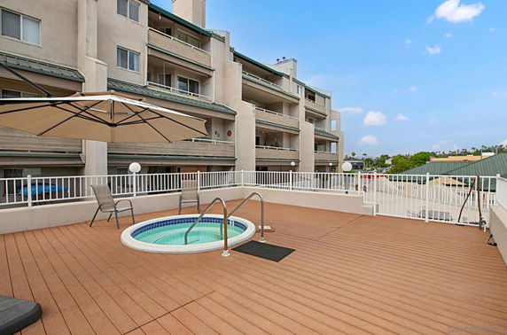 Rooftop area with a small circular swimming pool and umbrella seating, adjacent to a multi-story building.