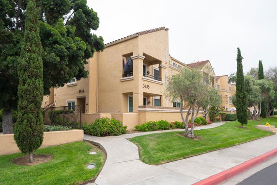 Front view of a beige multi-story apartment building with balconies and a landscaped walkway.