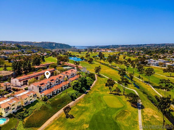 Aerial view of residential buildings adjacent to a golf course with scenic surroundings.
