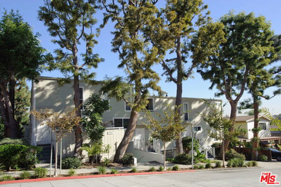 Front view of a multi-story house with trees and a staircase leading to the entrance.