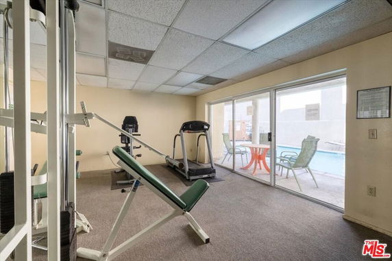 Room with gym equipment and exercise machines, adjacent to a pool visible through glass doors.