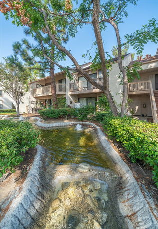 Front view of an apartment building with balconies and a small artificial pond in front.