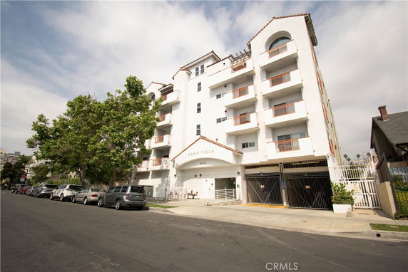 Front view of a multi-story apartment building with balconies and gated parking area.
