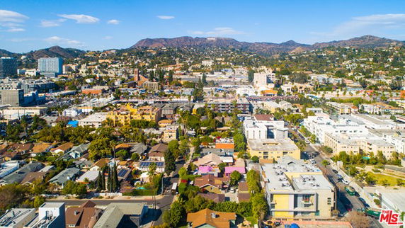 Aerial view of a cityscape with a mix of residential and commercial buildings, surrounded by hills.