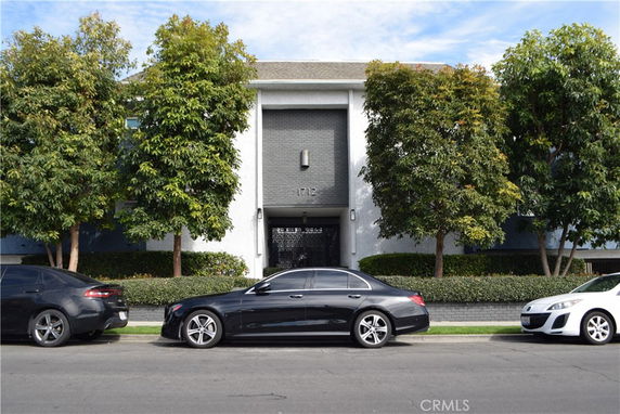 Front view of a two-story building with a central entrance, flanked by trees and parked cars on the street.