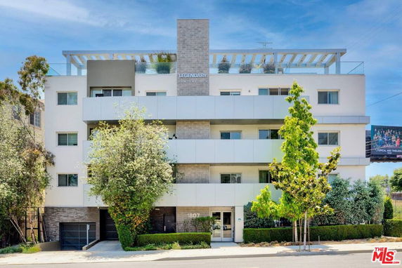 Front view of a multi-story apartment building with balconies and greenery.
