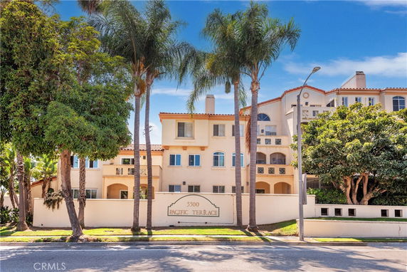 Front view of a multi-story residential building with balconies and palm trees.
