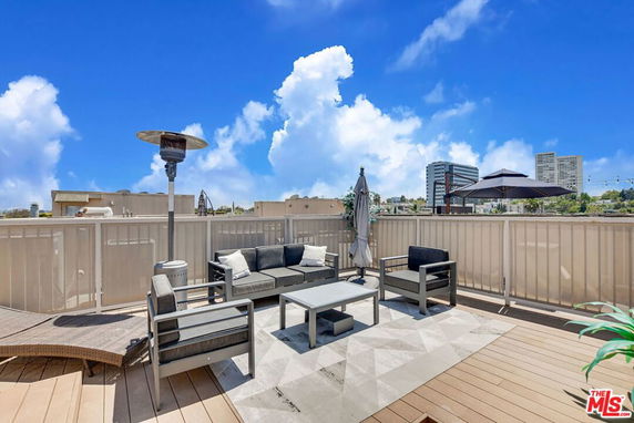 Rooftop area with seating and umbrella, with cityscape in the background.