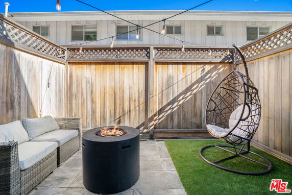 Outdoor patio area with wooden fencing, a wicker sofa, a hanging chair, and a fire pit.