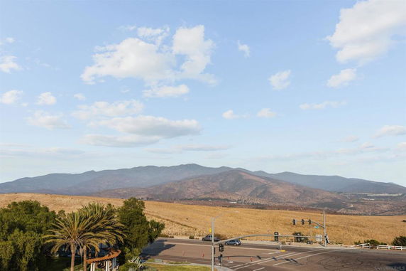 Panoramic view of rolling hills and a road intersection with traffic lights and trees in the foreground.