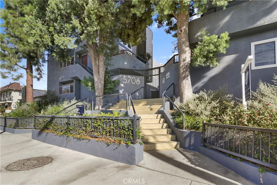 Front view of a multi-story building with stairs and a fenced entrance.