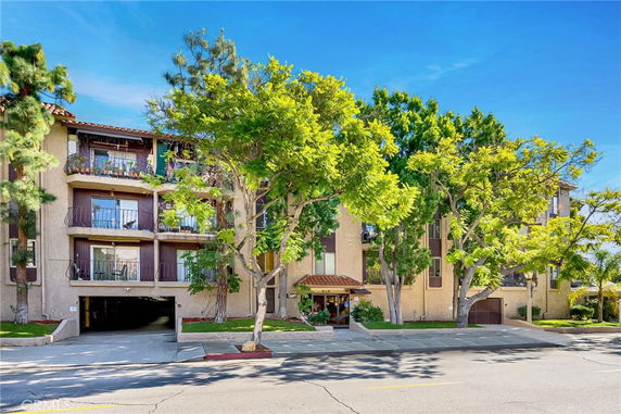 Front view of a multi-story residential building with balconies and trees in front.