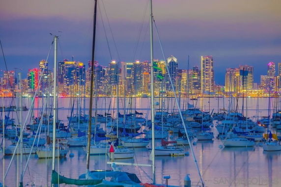 View of a marina with boats and a city skyline in the background during dusk.