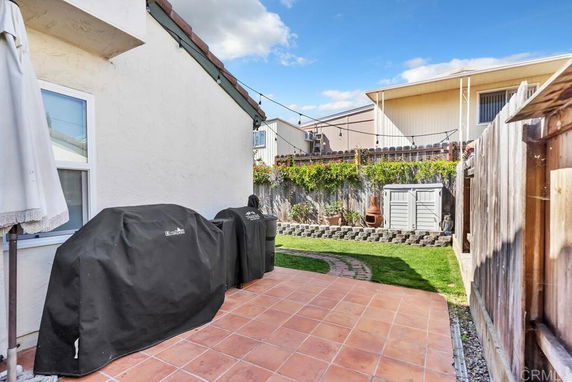Backyard view with tiled patio, covered grills, and a small storage shed.