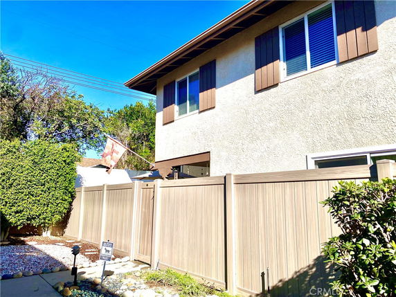 Side view of a two-story house with a wooden fence and window shutters.
