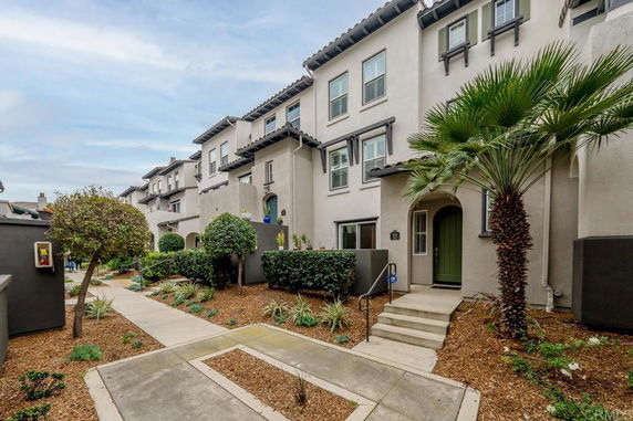 Front view of a multi-story townhouse with a green entrance door and landscaped front yard.
