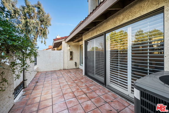 Outdoor terrace with large sliding glass doors and an air conditioning unit.
