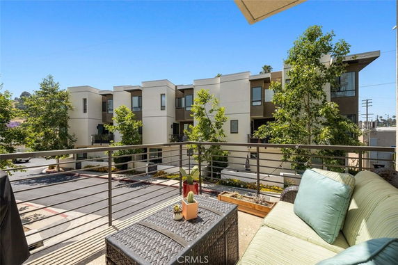 View of modern residential buildings and trees from a balcony with outdoor seating.