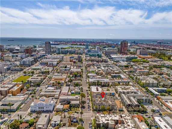 Aerial panoramic view of a coastal cityscape with residential and commercial buildings, and a harbor in the distance.