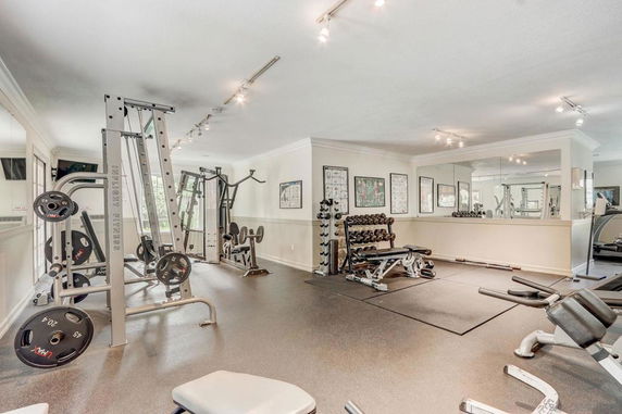 Gym area with weightlifting equipment and a mirrored wall.