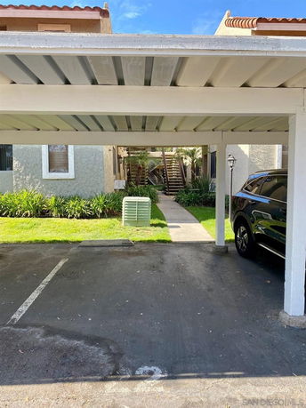 Covered outdoor parking area with a view of a multi-story building in the background.