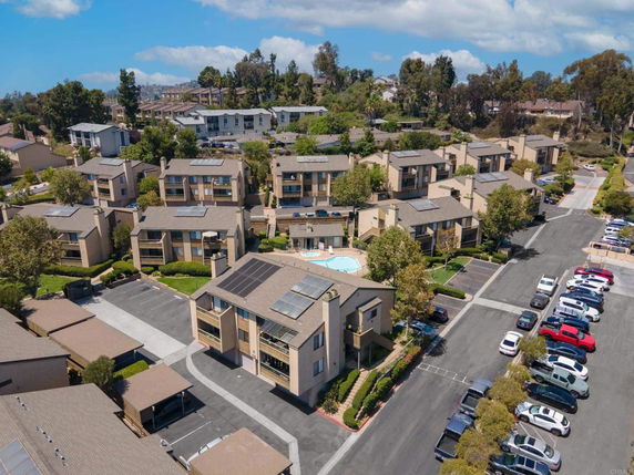 Aerial view of multiple apartment buildings surrounding a central swimming pool, with parking areas and landscaped greenery.