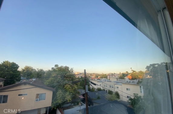 Panoramic view of a suburban area from a window, showing rooftops, trees, and expansive sky.