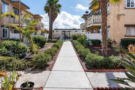Pathway leading to a gated area with multi-story residential buildings on either side and palm trees in the landscape.