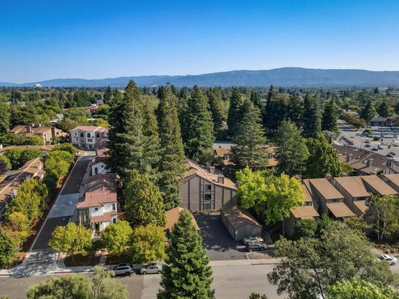 Panoramic view of residential buildings surrounded by trees and distant hills.