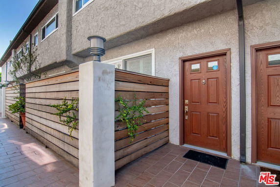 Front view of a townhouse with a wooden fence and a brown door.