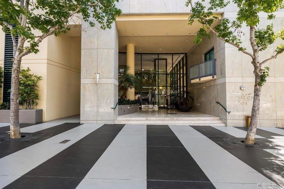 Front view of a modern building entrance with glass doors and trees lining the walkway.
