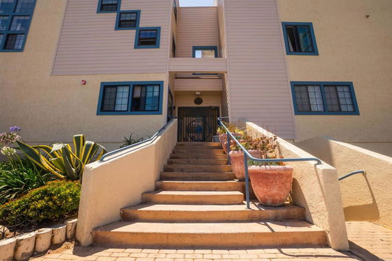 Entrance view of a multi-story building with blue-trimmed windows and a staircase leading up to the entrance.