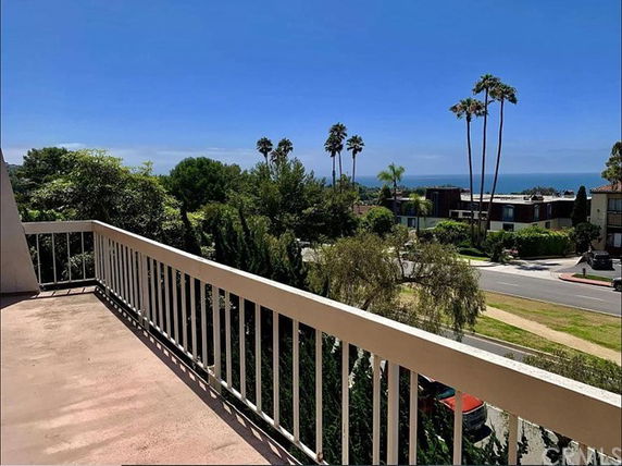 Panoramic view from a balcony overlooking trees and the ocean in the distance.