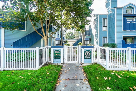 Front view of a residential building with blue siding, white fencing, and outdoor stairs.