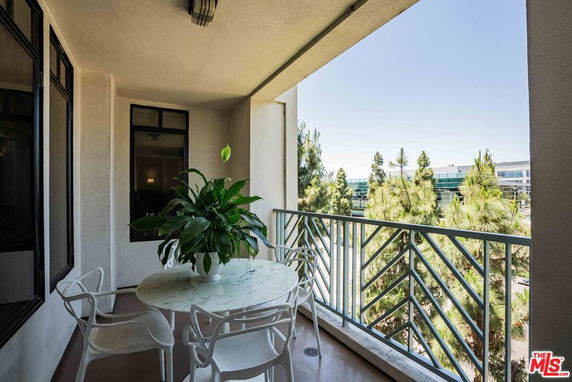 Outdoor balcony area with a table and chairs, view of trees and buildings in the background.