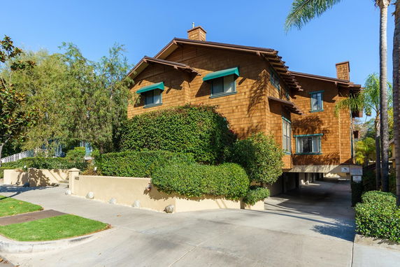 Front view of a multi-story wooden house with green awnings and surrounding greenery.