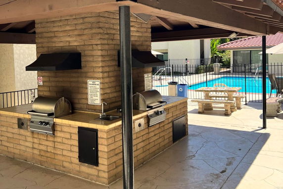 Outdoor swimming pool area with barbecue grills and picnic tables.