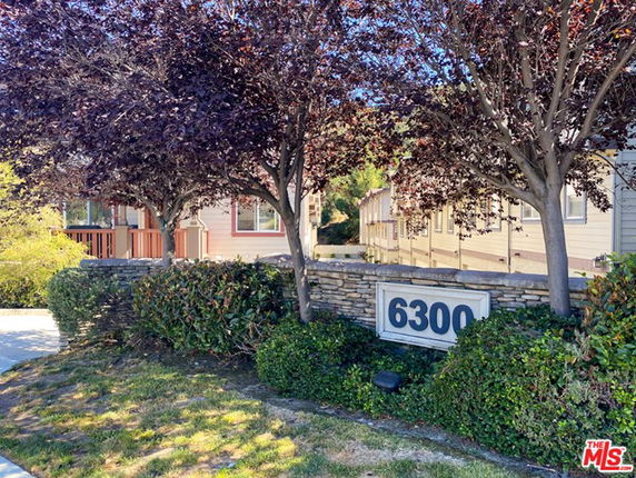 Front view of a residential building with stone fence and trees.