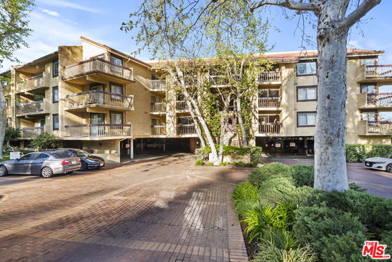 Front view of a multi-story residential building with balconies and brick driveway.