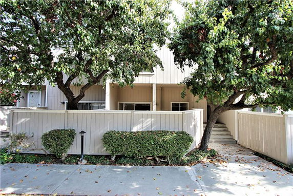 Front view of a two-story house with a fence and surrounding trees.