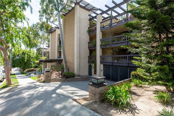 Front view of a multi-story apartment building with balconies and surrounding greenery.