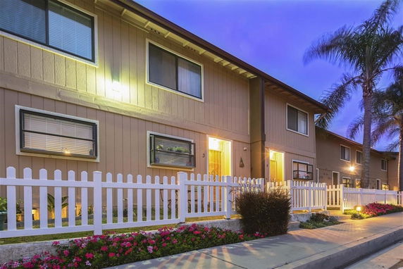Front view of a multi-story residential building with white picket fence.