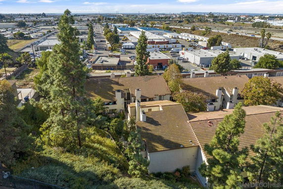 Aerial view of buildings with tan roofs surrounded by trees, overlooking a larger industrial area with warehouses.