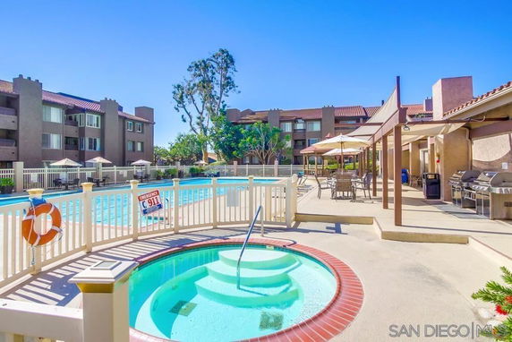 Outdoor swimming pool area with surrounding fence, umbrellas, and a nearby building.