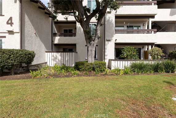 Front view of a multi-story building with balconies and a tree in front.